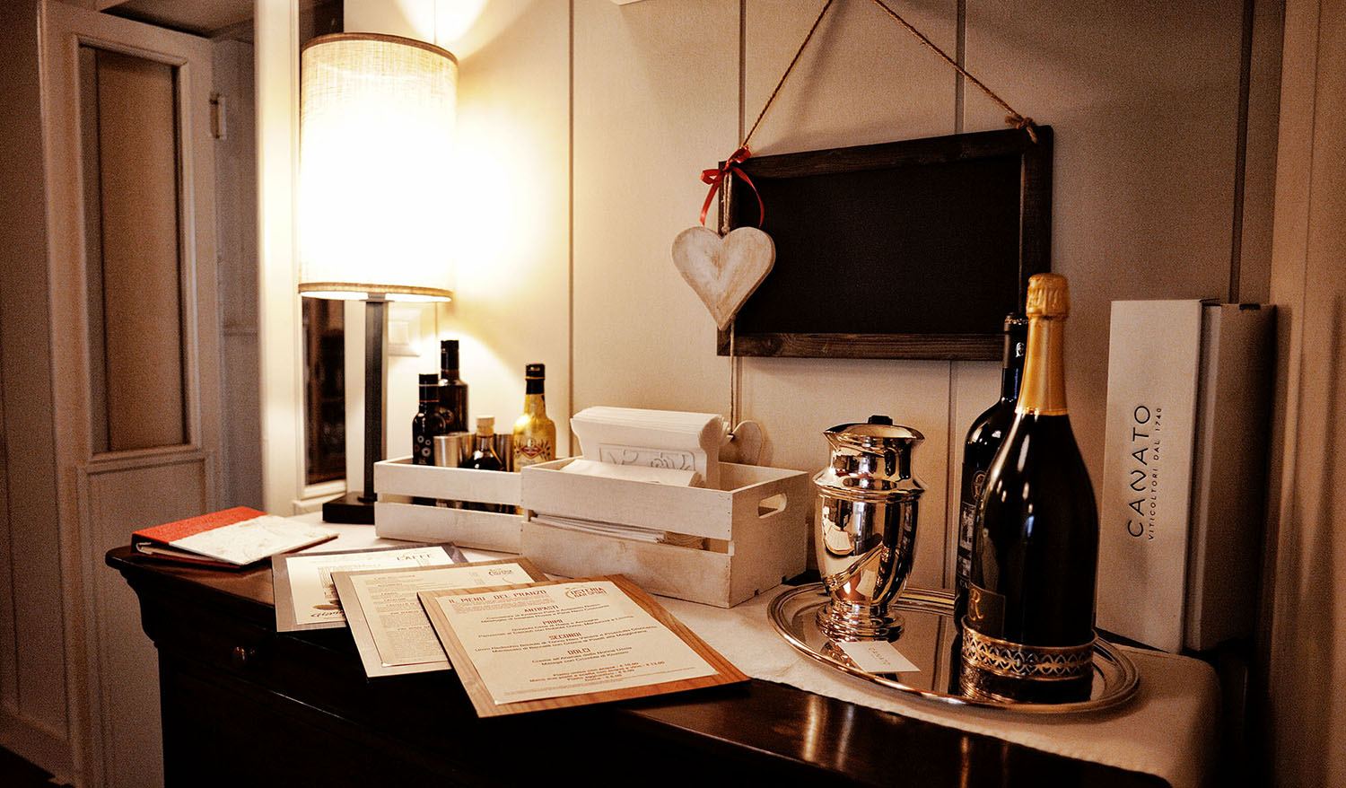 La credenza con i menù del giorno, una lampada e le bottiglie di vino