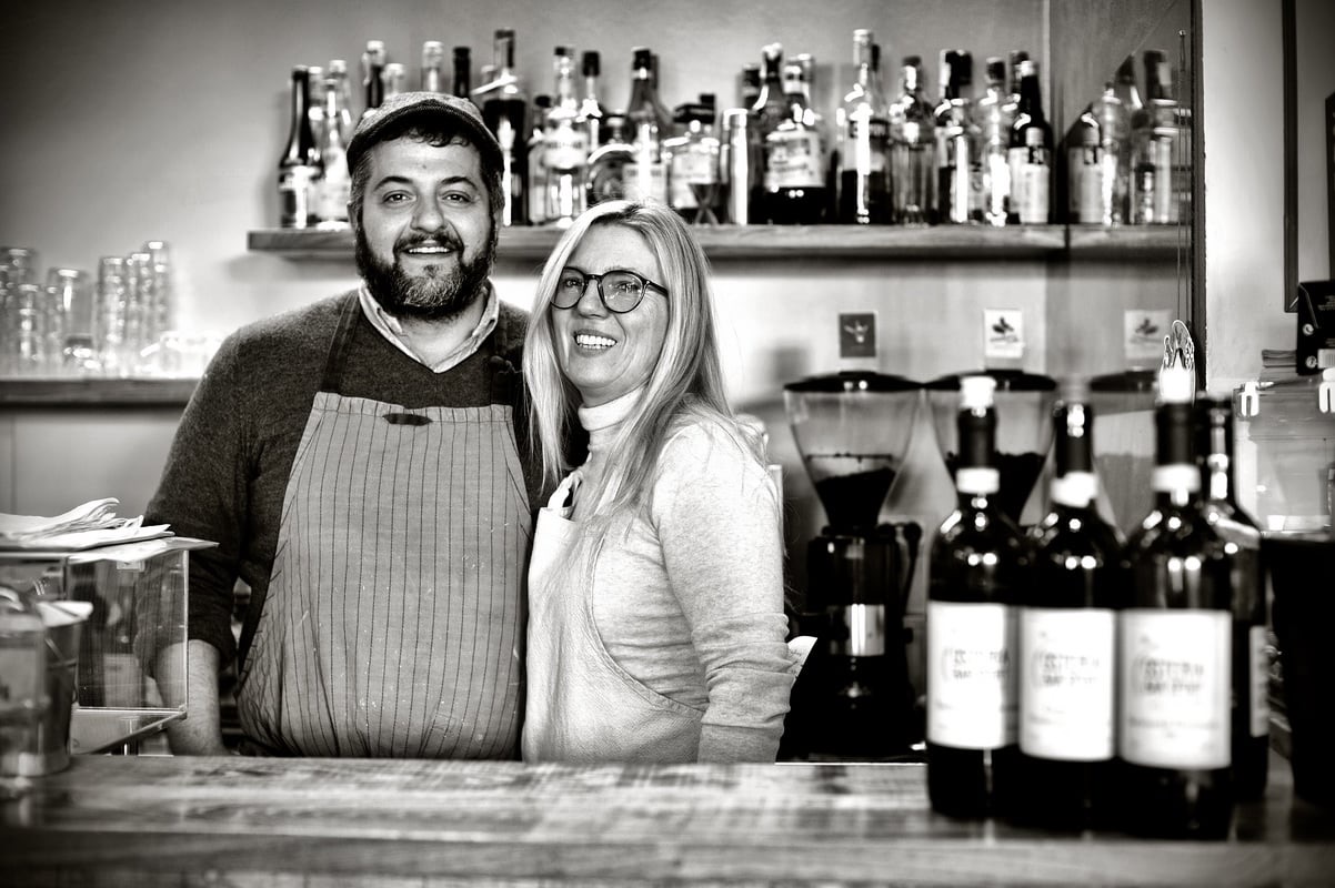 Paola Brovero e Tommaso Negri sorridenti dietro al bancone dell'osteria